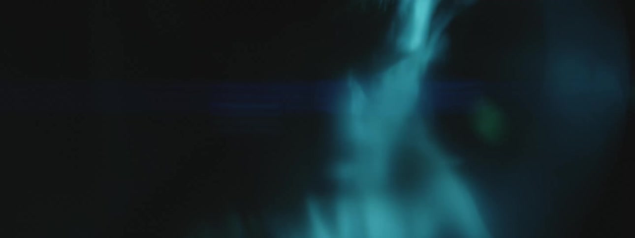 A male turns his head while smoke escapes from his mouth while he is in a dark setting