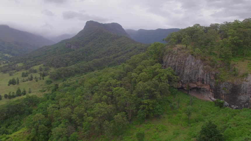 Fog covers mountains bordered by valley slopes covered by forest