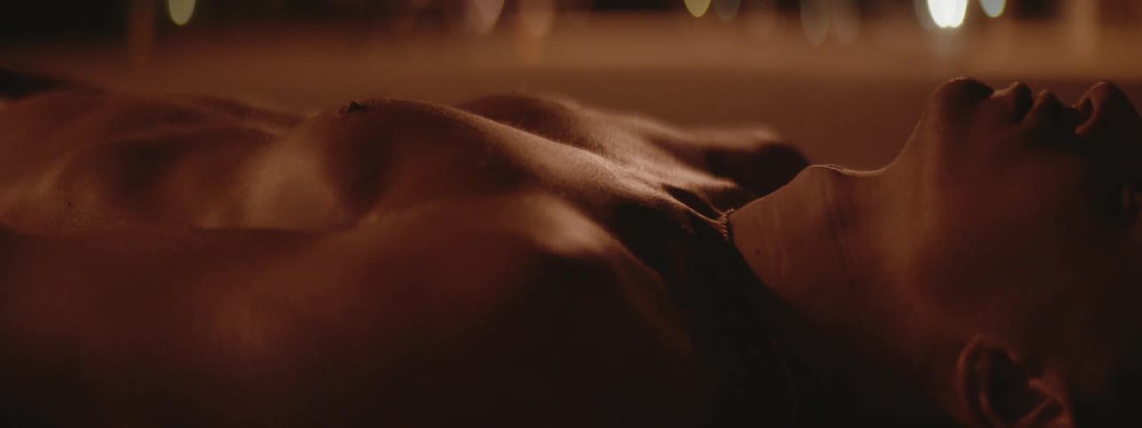 A teenage boy lies on the ground outside and takes deep breaths and lights flicker in the distance
