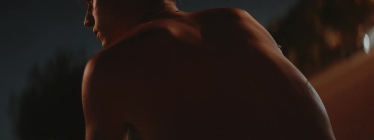 Back of a shirtless young man sitting at the side of a road at night