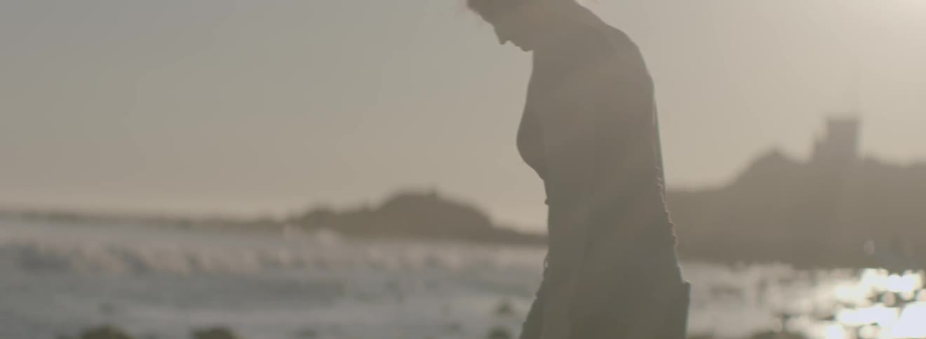A woman leans forward over some rocks on a beach
