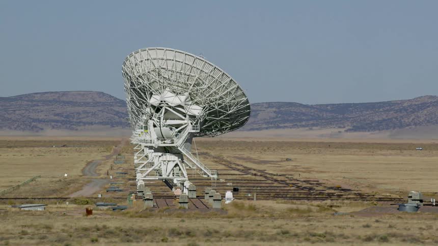 A landscape with satellite dishes with a mountain range the sky and clouds in the background