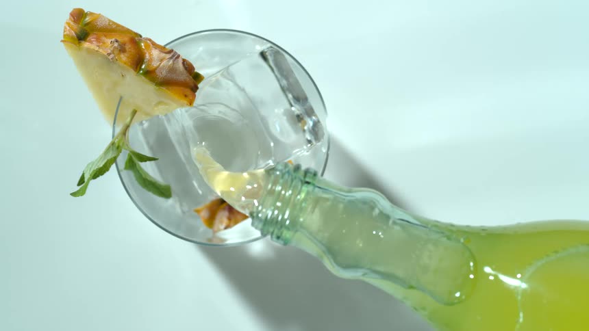 Alcohol being poured into a glass with fruit and ice from a bottle