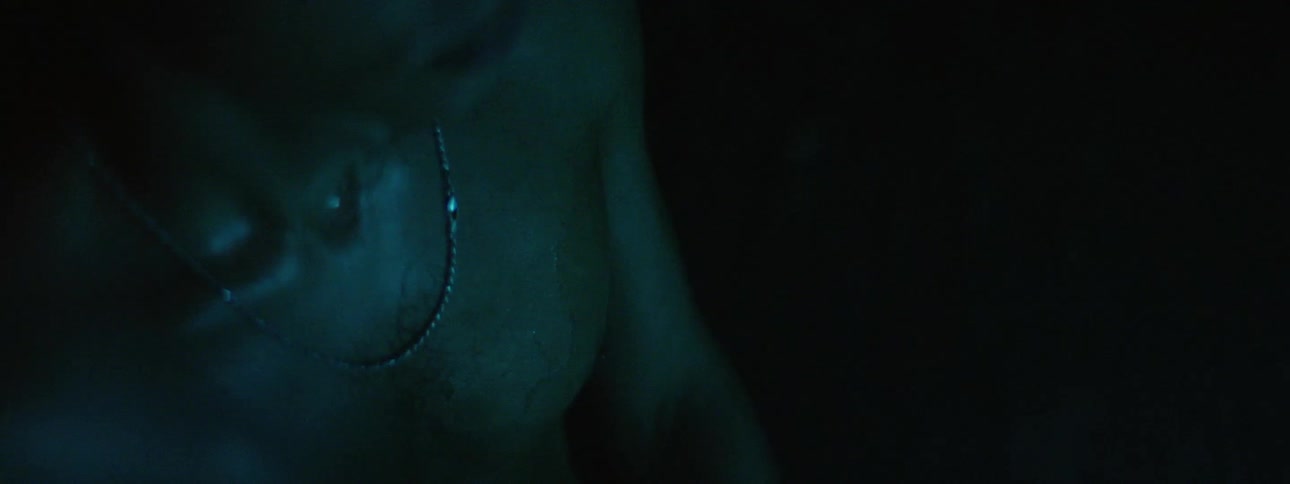 A glowing green light passes over a shirtless man causing his skin to glisten