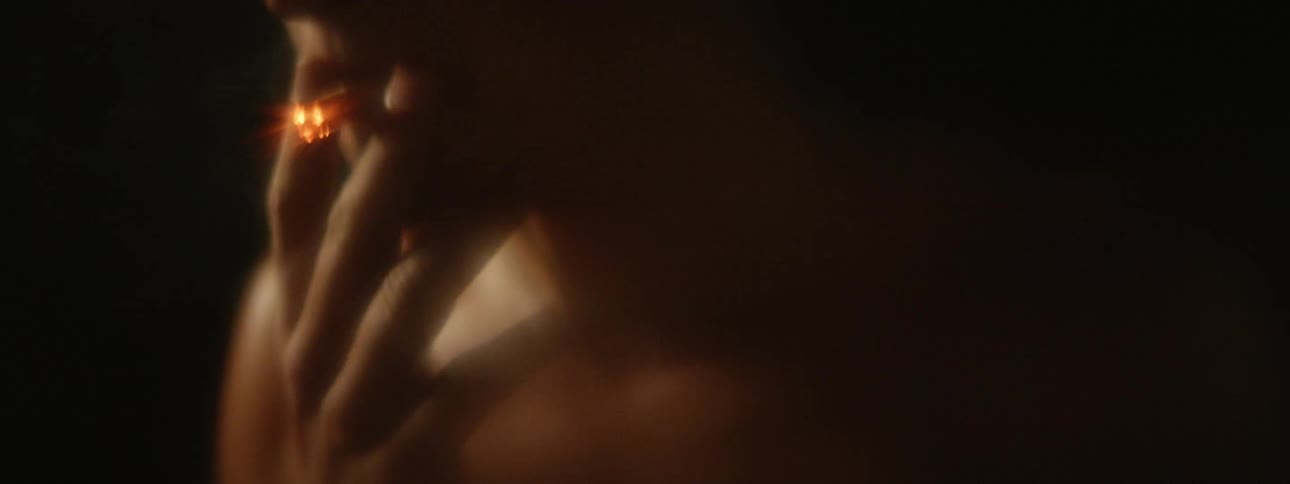 Young shirtless person lighting a cigarette with a lighter and blowing smoke