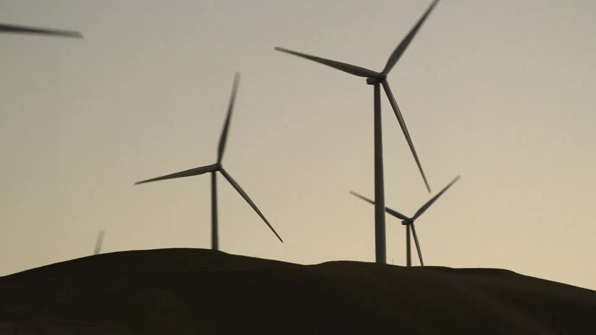 Blades of wind turbines turn slowly in wind farm sitting on hill