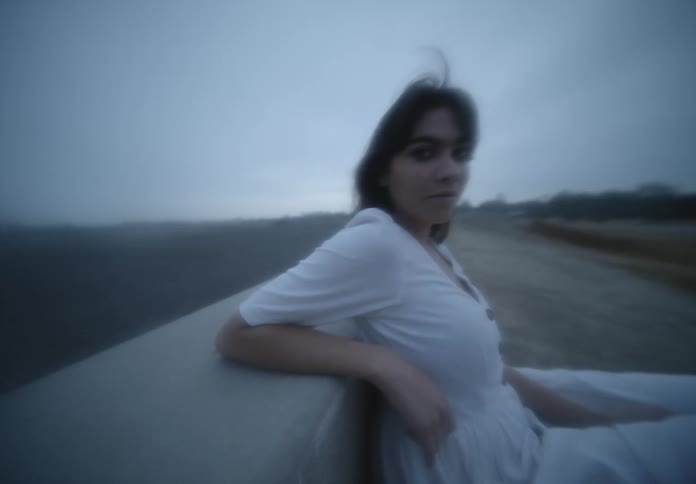 A woman with a dress staring with trees the sky and clouds in the background