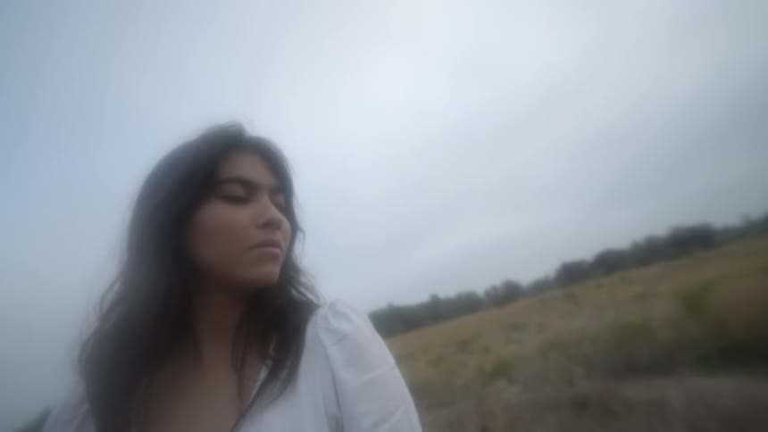A woman sits with her eyes closed on a hill slope on a cloudy day