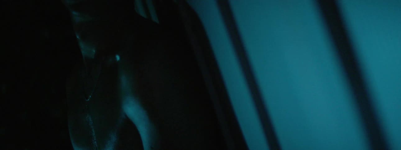 A light flashes over a shirtless man leaning against a wall causing his skin to glisten