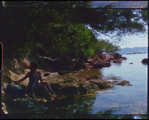 A woman sits on rocks along the edge of a lake