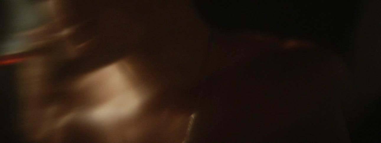 Bare chested young man lights a cigarette and blows smoke inside a dark room