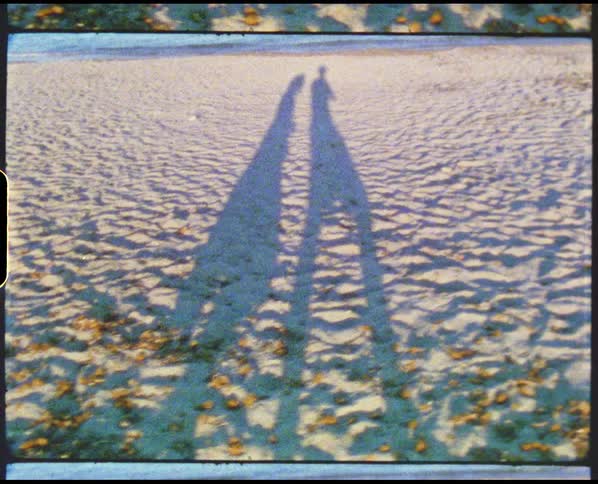 Tall shadows of two people walking on a sandy beach