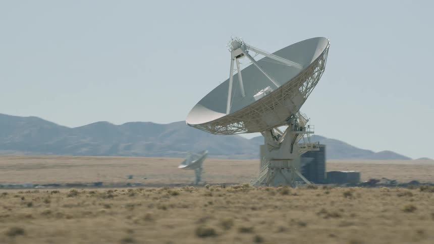 A landscape with satellite dishes with a mountain range the sky and clouds in the background