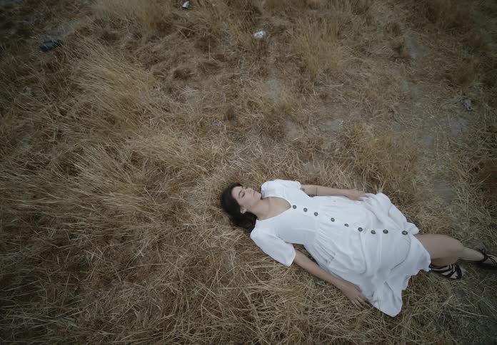 A woman in a white dress lays on her back in a grassy field while seemingly asleep