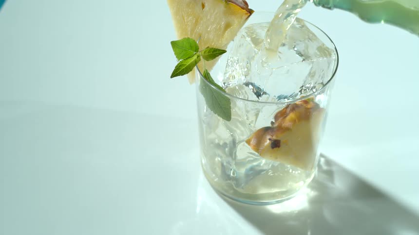 A beverage being poured in to a glass with ice and pineapple for a photo shoot