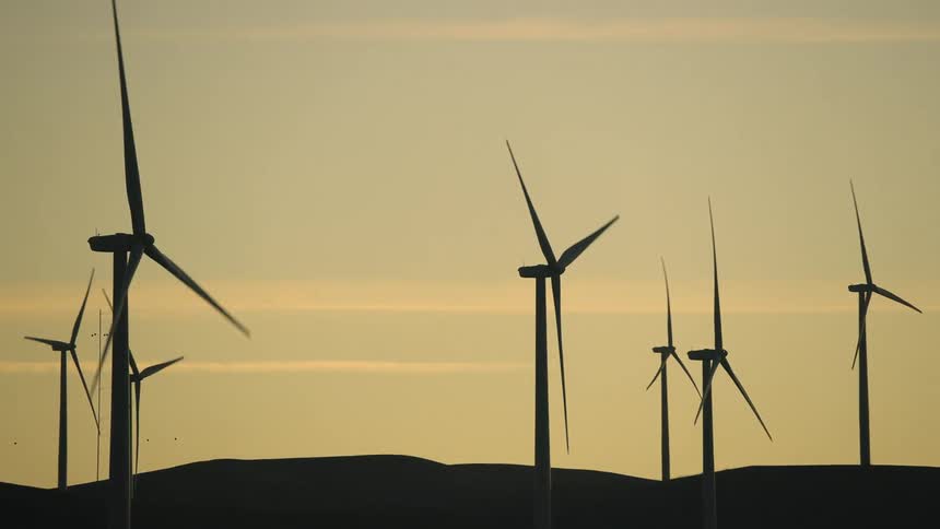 The silhouette of several wind turbines against a yellow sky