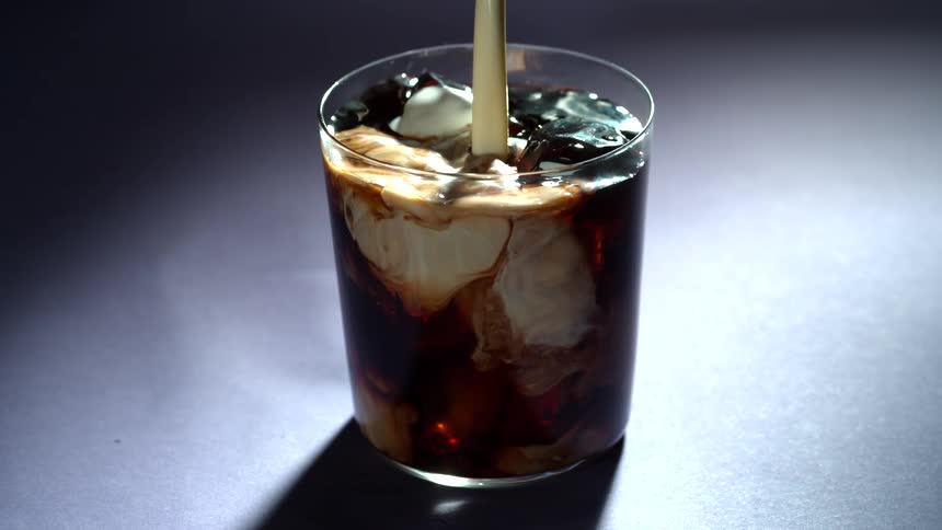 Creamer is pouring into a glass of iced coffee