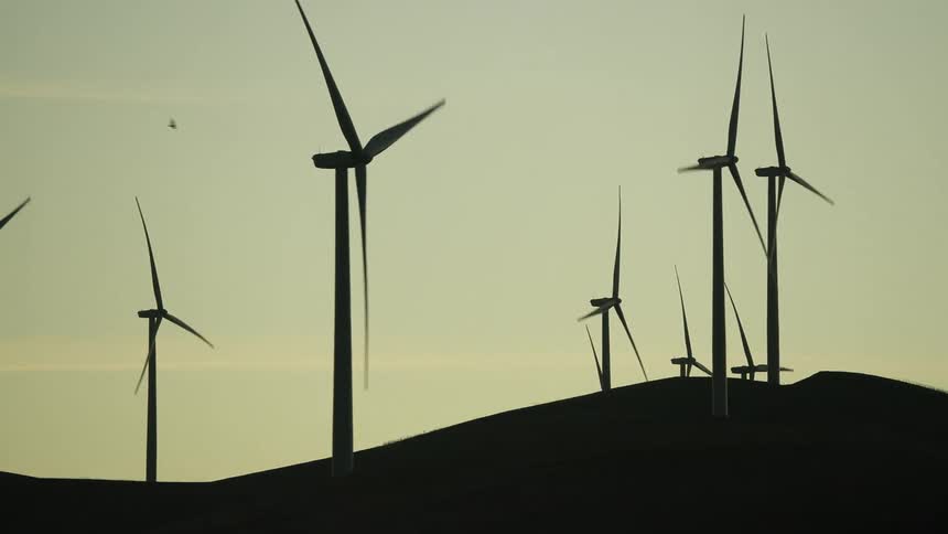 A landscape with silhouettes of wind turbines with the sky and clouds in the background