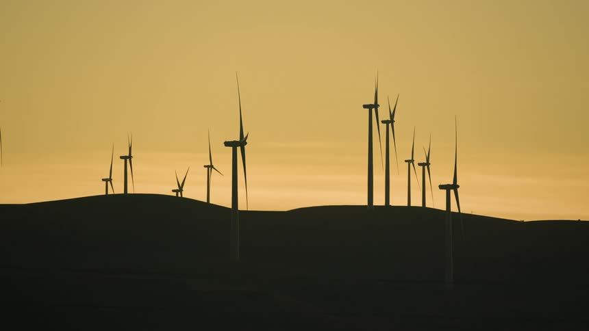 Wind turbines spin on a wind farm in a hilly landscape at sunset