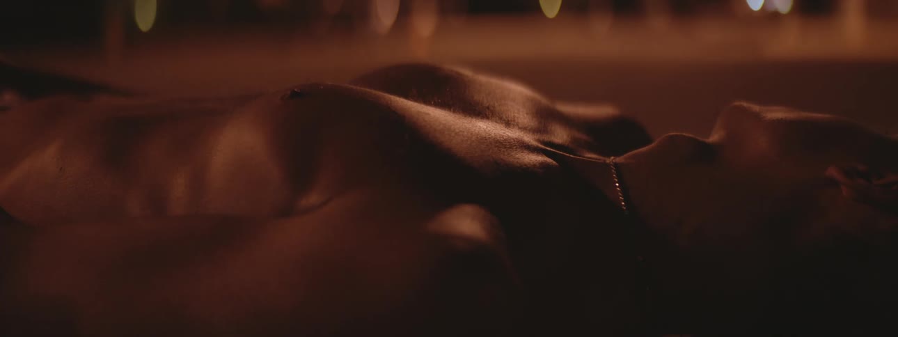 Shirtless man with necklace lying down on ground inhales deeply