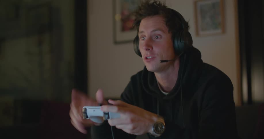 A man talks on a headset and gestures with his hand as he plays a video game