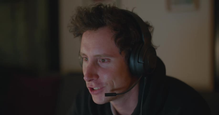 Young man sitting on a room in front of a screen talking on a headset
