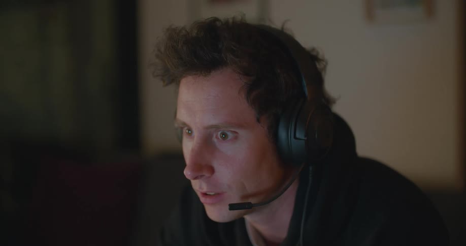 A young man sits on a couch at home and talks in to a headset