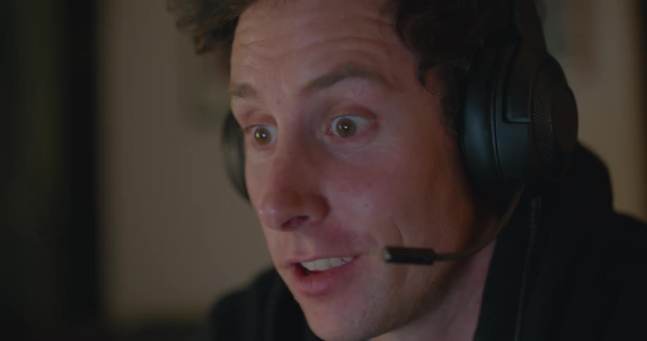 A man in a room with a headset and videogame controls with a wall in the background