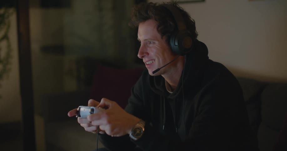 Young man sitting in the couch at home wearing headphones playing video games with a controller