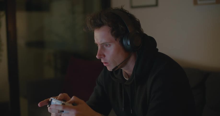 Man with headphones and black hoodie holds game controller and plays game on television