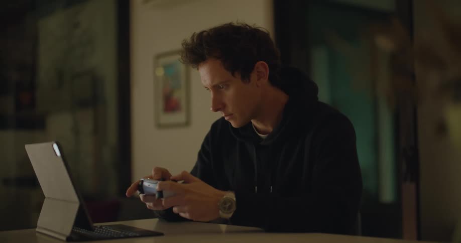 Man sits at table gaming with wireless game controller and tablet