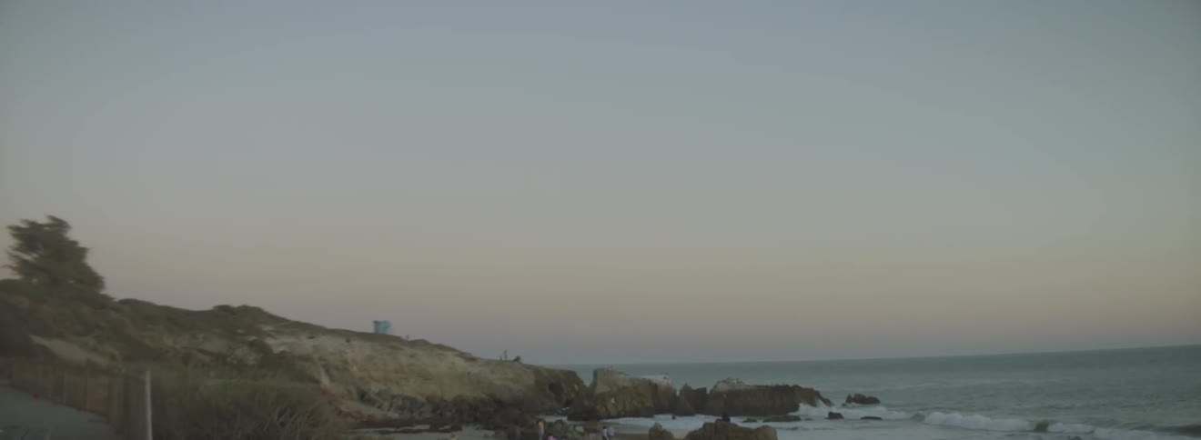 Waves crash against the rocks of a shore at sunset
