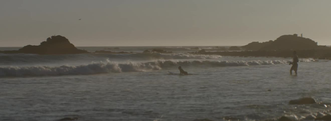 A man watches as another moves into the waves on a surfboard
