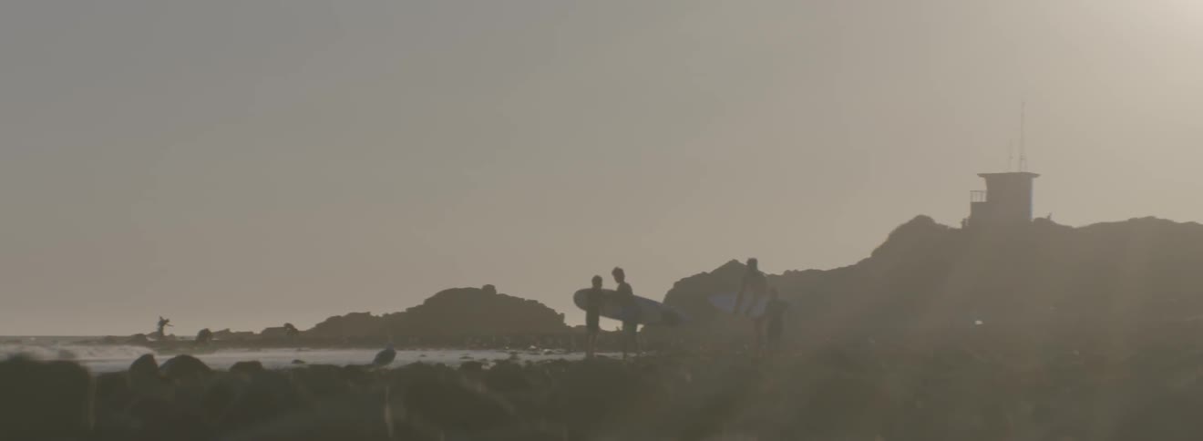 Two boys holding surfboards as they stand with other boys next to the ocean