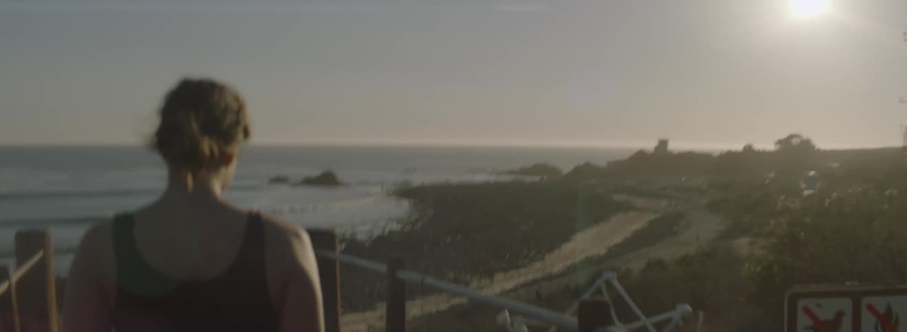 A woman in a sleeveless shirt walks toward a beach