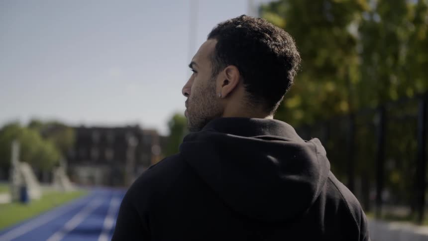 A person in a black hoodie looks around at a track