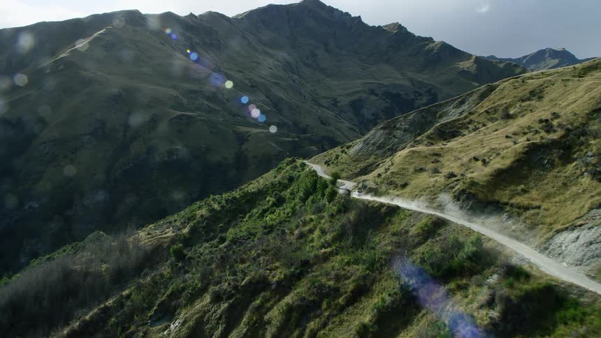 A vehicle travels along a mountain pass on a verdant mountain during the day