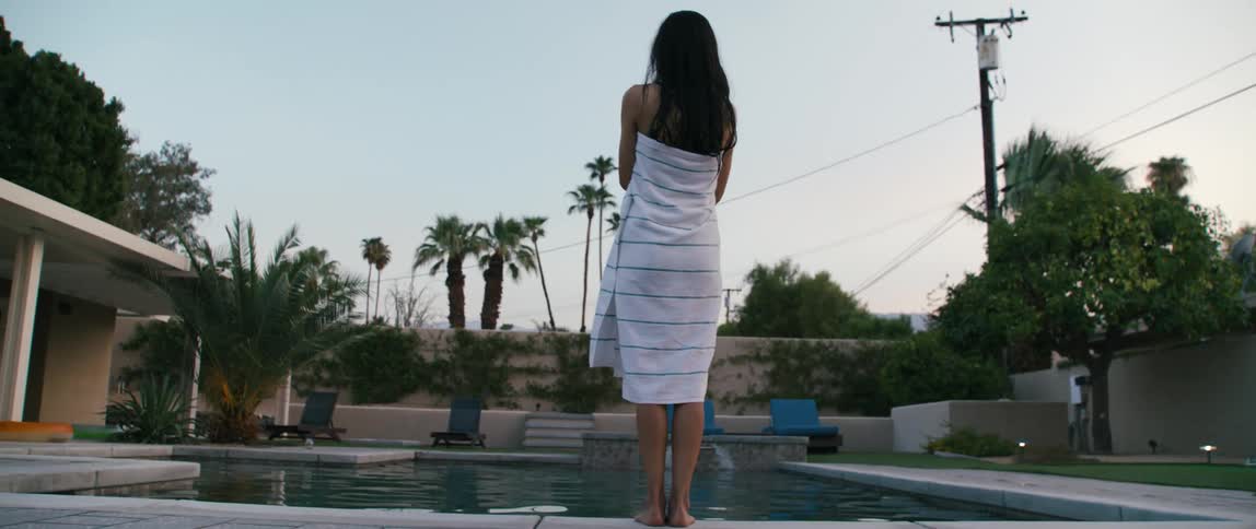 A woman stands by a pool outside with a towel around her