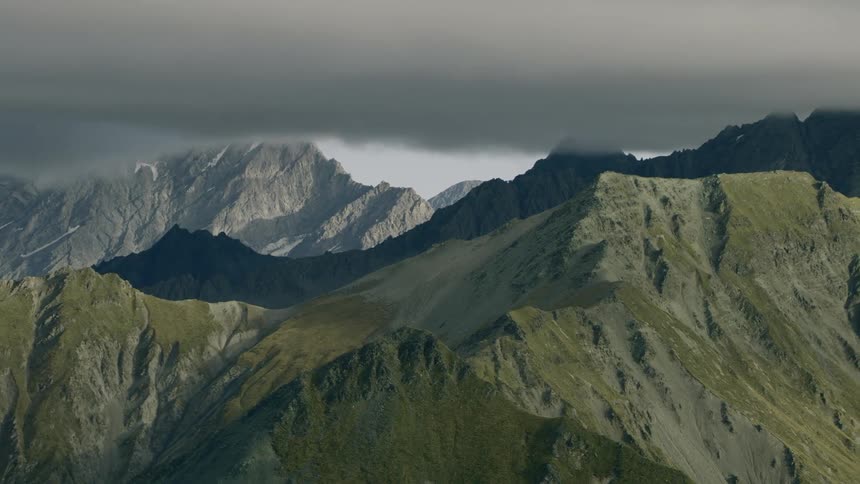 A thick layer of clouds hovering over a green mountain range
