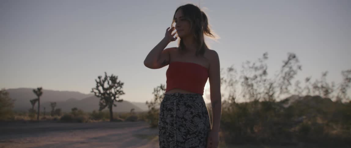A woman poses in a field with her hand held next to her head