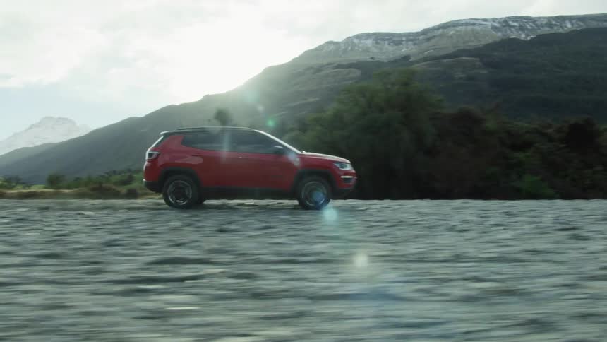 A vehicle driving offroad with trees a mountain range the sky and clouds in the background
