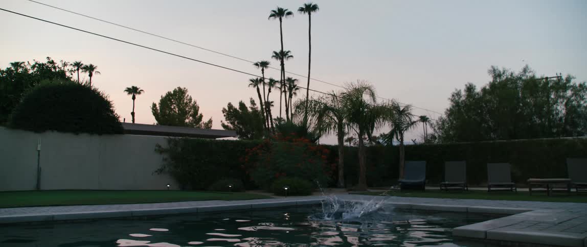 A woman diving into a pool with a wall trees the sky and clouds in the background