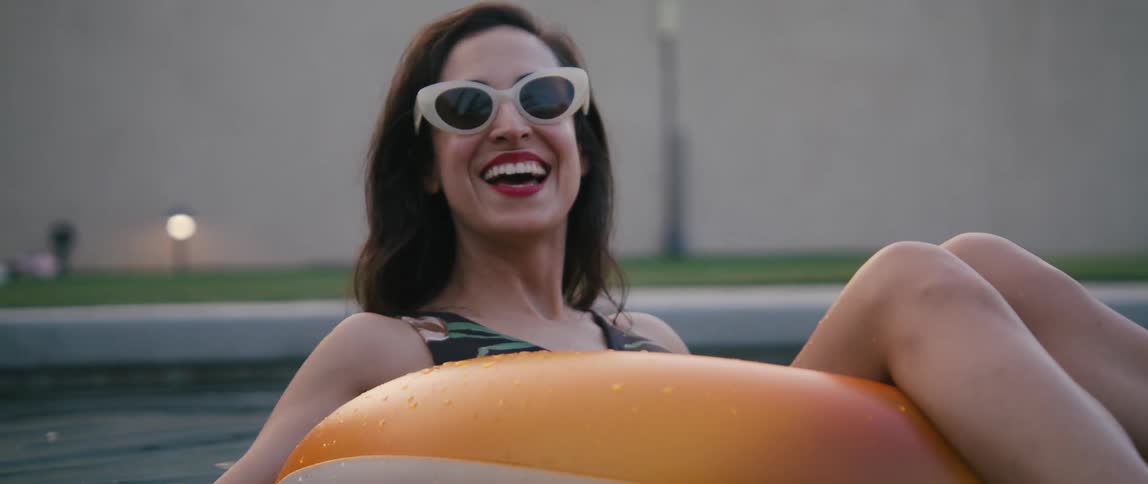 Woman wearing sunglasses laughs and smiles while floating on a pool