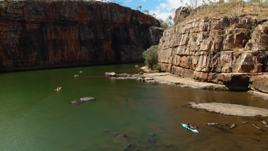 A group of kayakers travel along a river through a canyon during the day