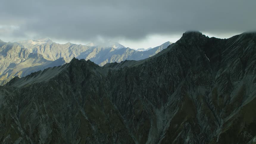 Aerial view of the peaks on a mountain range under the shadow of the clouds