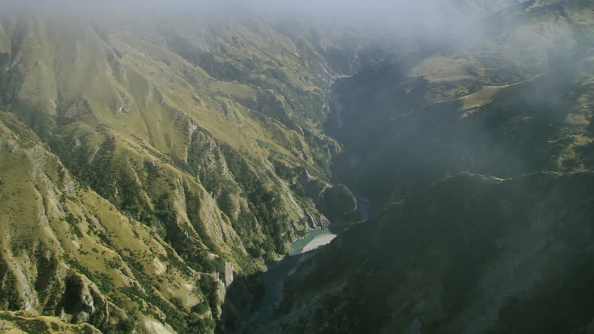 An aerial view of fogs over a river running through a mountain range