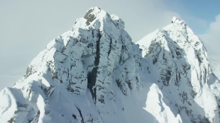 Snow covers twin peaks and surrounding mountains under a cloudy sky
