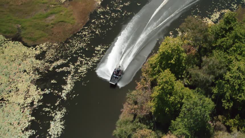 People are traveling on an airboat on a muddy river on a sunny day