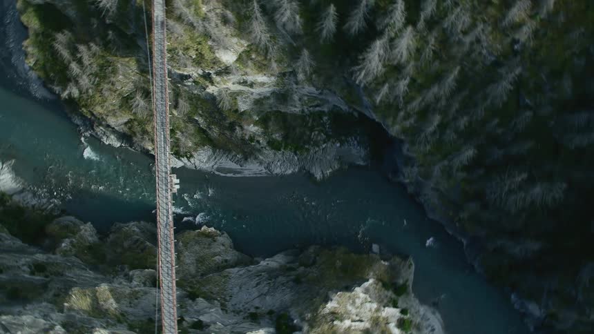 Aerial view of a metallic suspension bridge over the river in a canyon