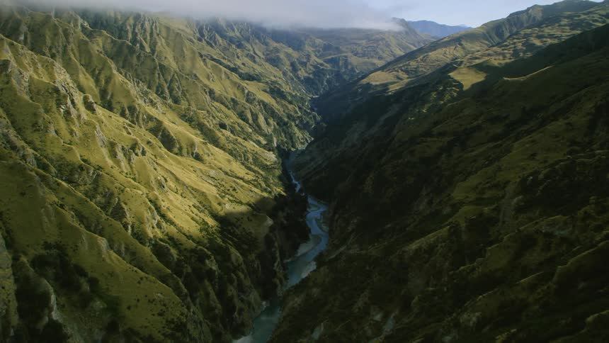 A river runs along the floor of a narrow valley between mountains during the day